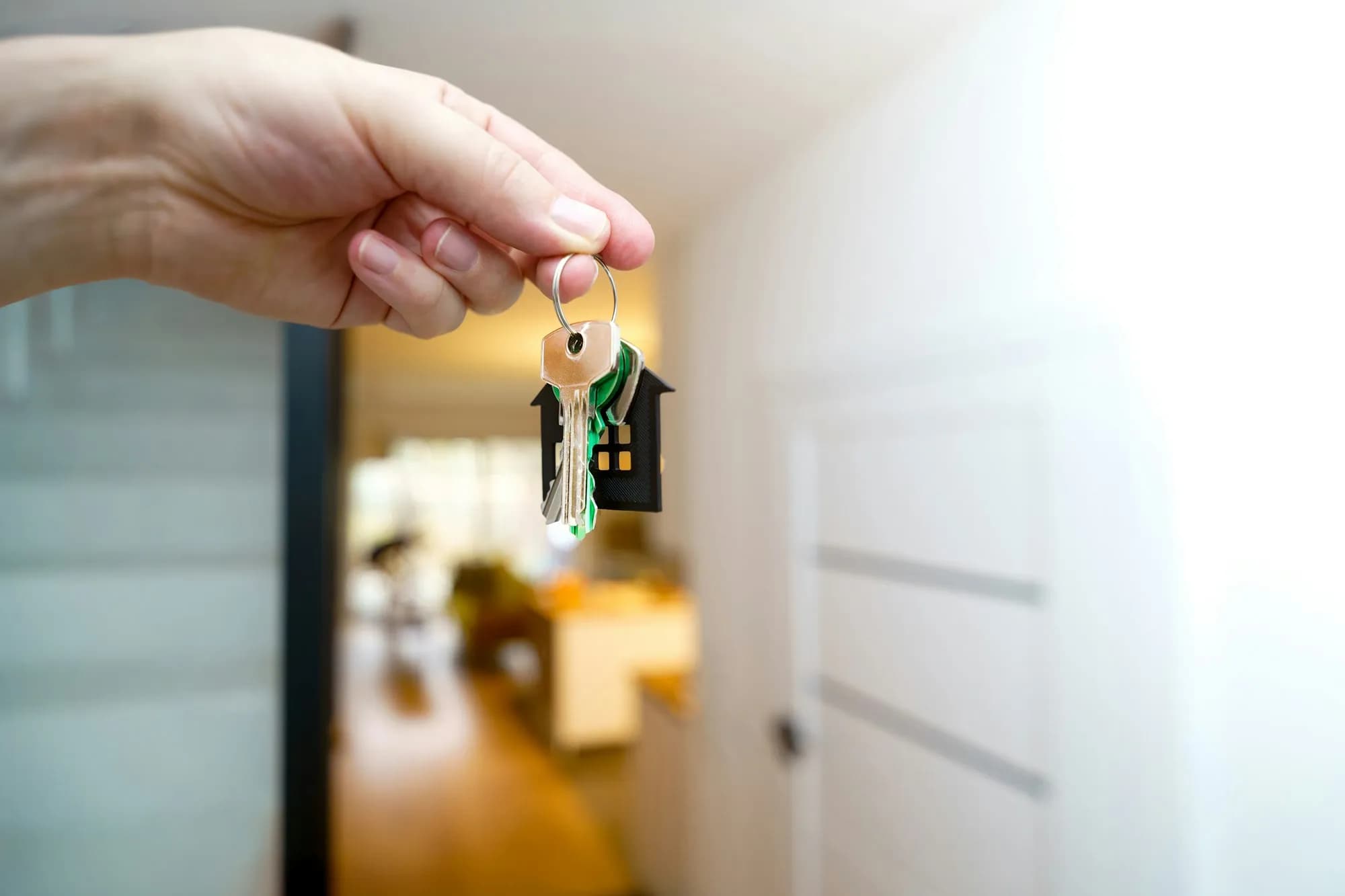 Hand hält einen Schlüsselbund mit Hausanhänger vor einer geöffneten Wohnungstür
