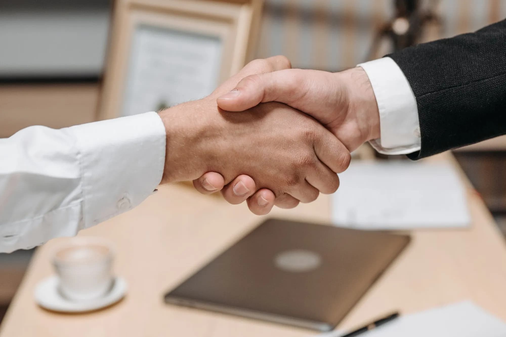 Handschlag zwischen zwei Personen über einem Schreibtisch
