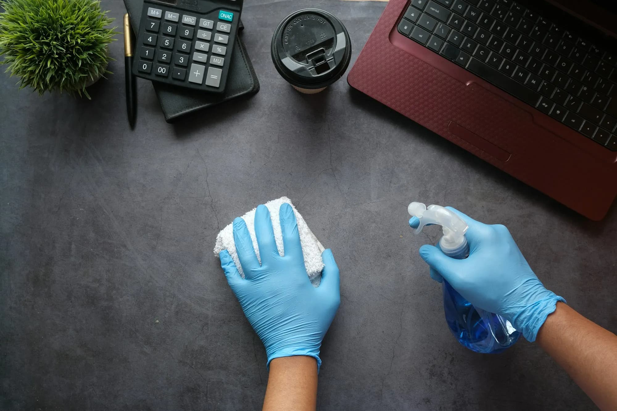 Hände in Handschuhen wischen einen Schreibtisch ab
