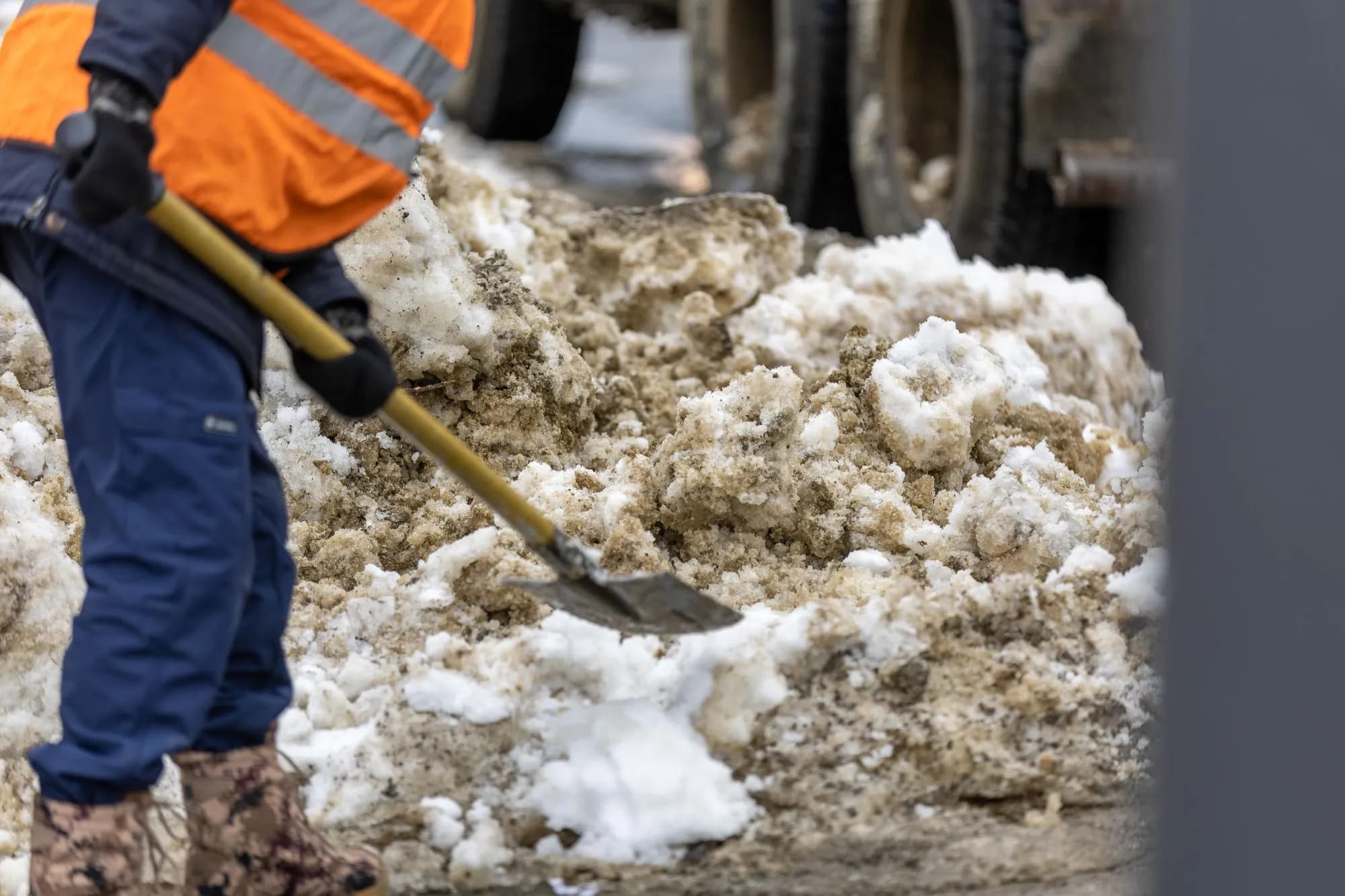 Person in Warnweste schaufelt Schnee von einem Gehweg